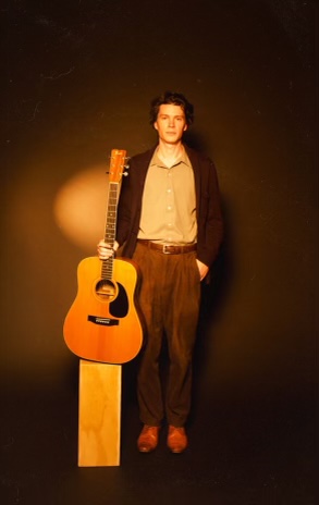 Kyler J standing beside his acoustic guitar