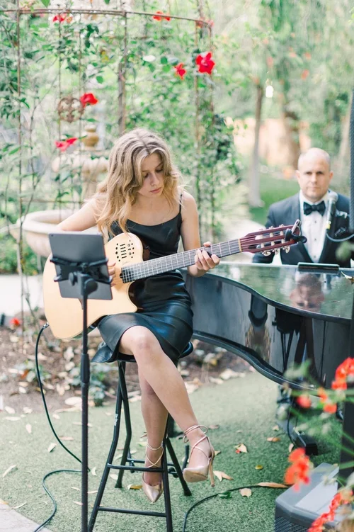 Kateland Raftery playing guitar with a pianist at an outdoor wedding